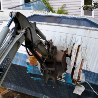 Excavator tearing into an old boat during vehicle demolition in Rhode Island – includes RV and mobile home removal services